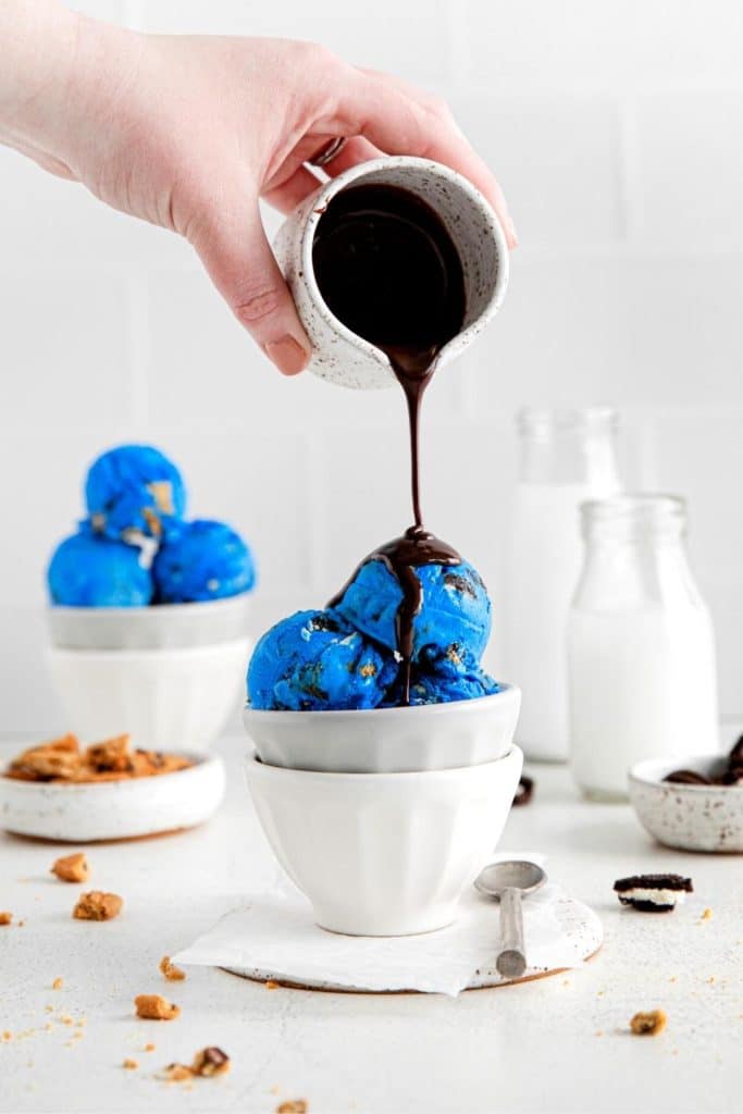 Hot fudge actively drizzled over a 3-scoop serving of blue cookie monster ice cream.