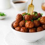 Serving bowl of appetizer meatballs with the tines of a fork digging in.
