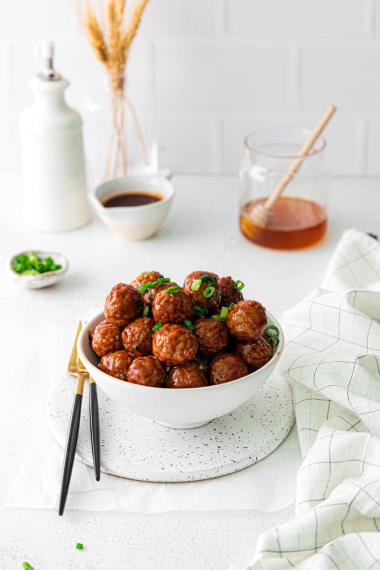 Bowl of crockpot BBQ meatballs garnished with green onions on an appetizer table with forks.