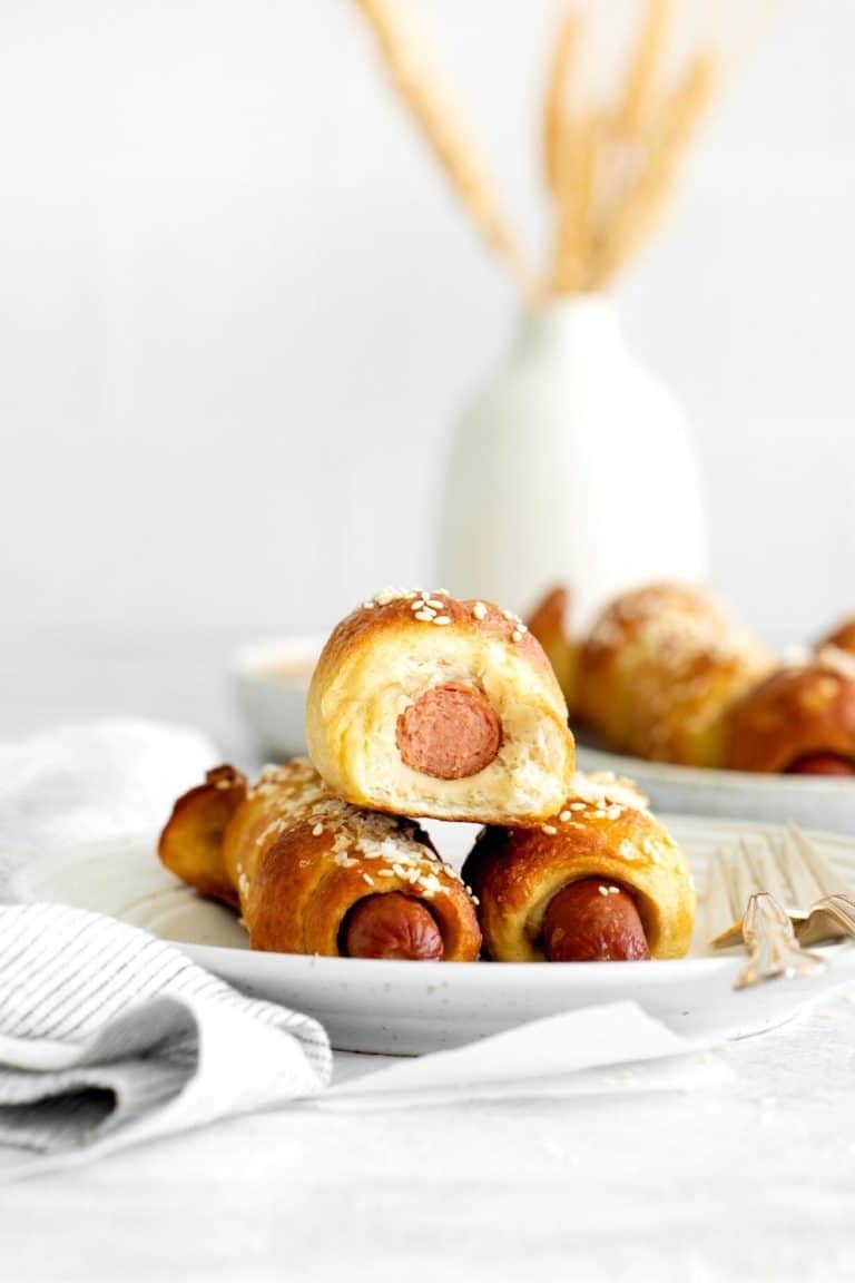 Three pretzel dogs on a plate with a bite taken out of one.