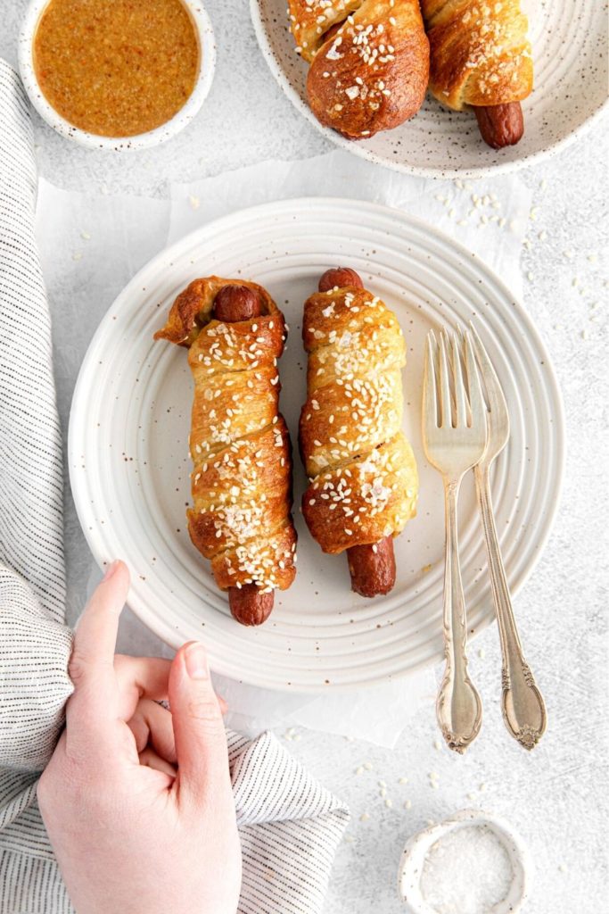 Hand setting down a plate with 2 pretzel dogs next to honey mustard dipping sauce.