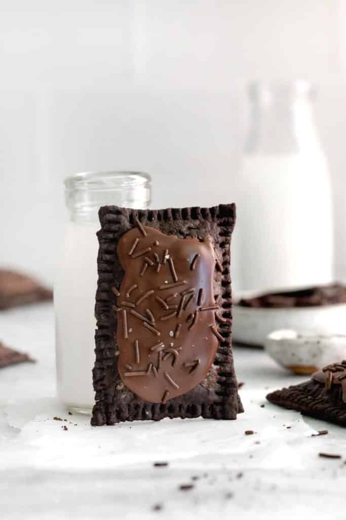 A chocolate pop tart propped up against a glass bottle of milk.