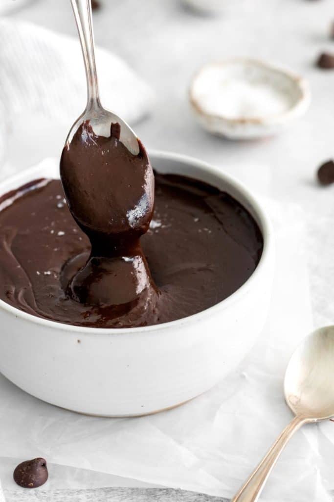 Hot fudge sauce dripping down into a bowl from a spoon.