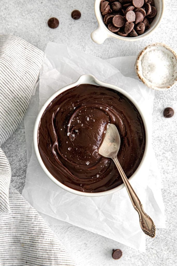 Thick homemade hot fudge sauce in a bowl garnished with a pinch of flaky sea salt.