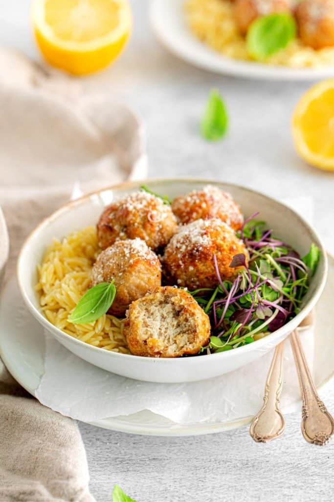 Five lemon butter chicken meatballs served in a bowl with a bite taken out of one.
