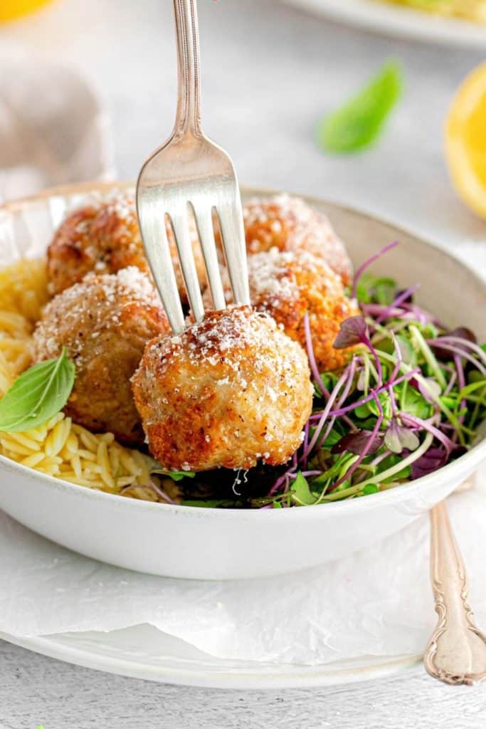 The tines of a silver fork piercing an air fryer chicken meatball.