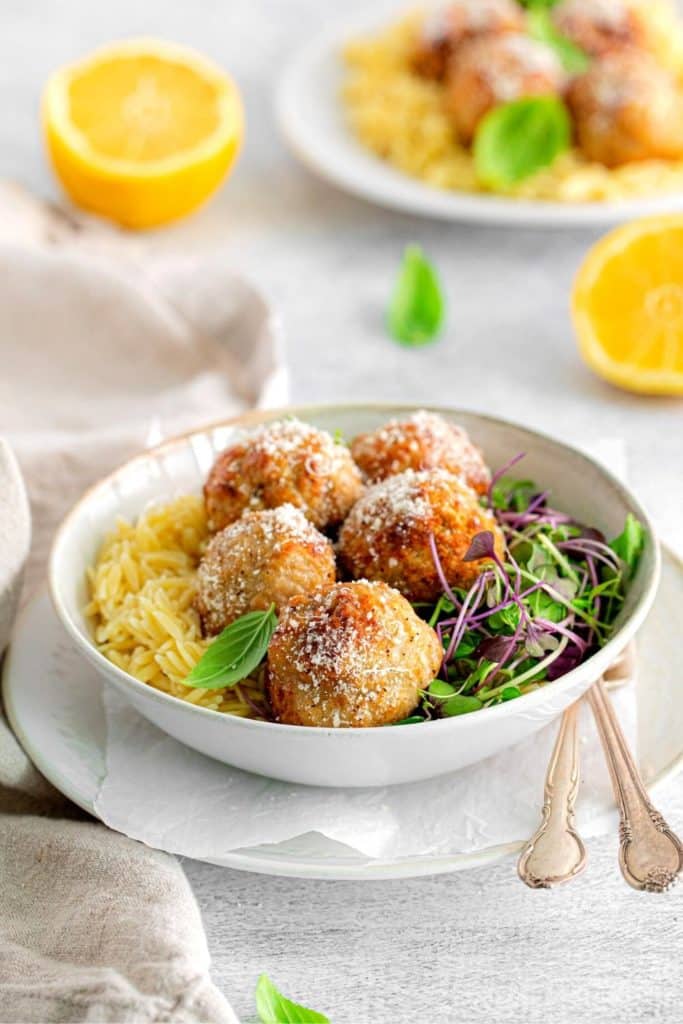 Chicken meatballs and orzo plated in a wide bowl with microgreens.