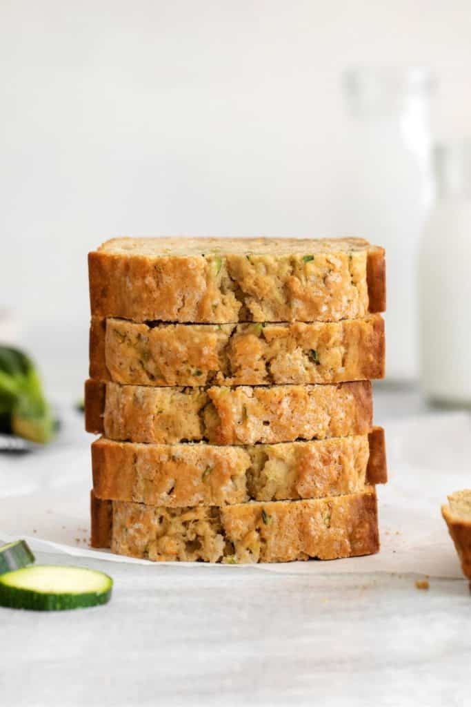 Five slices of Mom's zucchini bread stacked on a serving table with 2 glass bottles of milk.