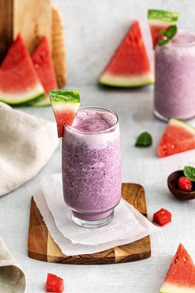 A berry watermelon smoothie with a frosty texture in a glass garnished with a wedge of watermelon.