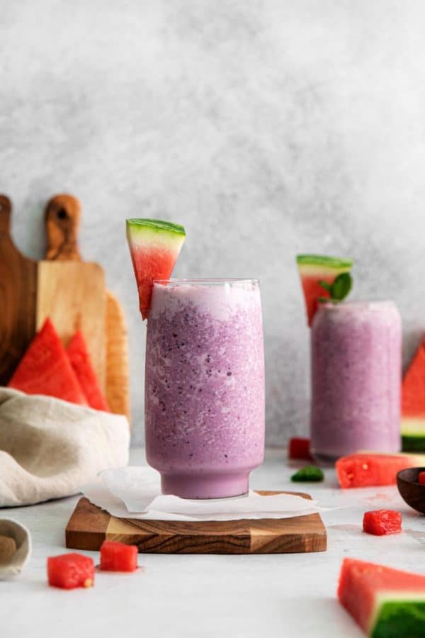 Watermelon berry smoothie in a tall glass garnished with a wedge of fresh watermelon.
