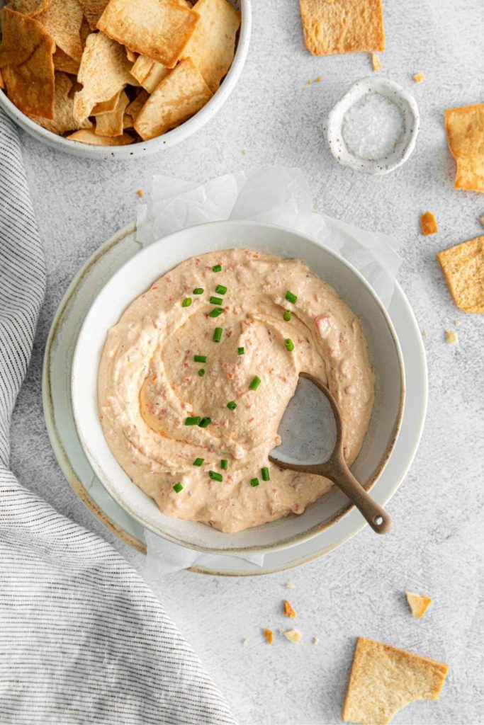 Red pepper feta dip being scooped from an appetizer bowl with a spoon.
