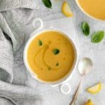Summer squash soup served in a white handled soup bowl with a silver soup spoon.