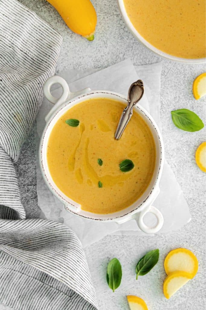 Soup with yellow squash garnished with a drizzle of olive oil and fresh herbs.