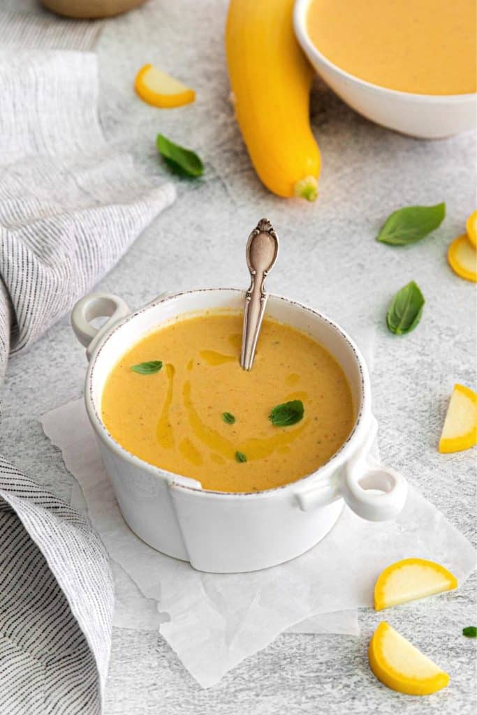 Yellow squash soup served in a special white handled soup bowl with a spoon.
