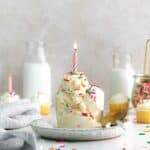 Two scoops of birthday cake ice cream in a small glass dessert cup with lit birthday candle.