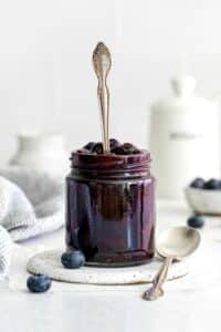 Homemade blueberry pie filling in a glass jar with silver spoon.