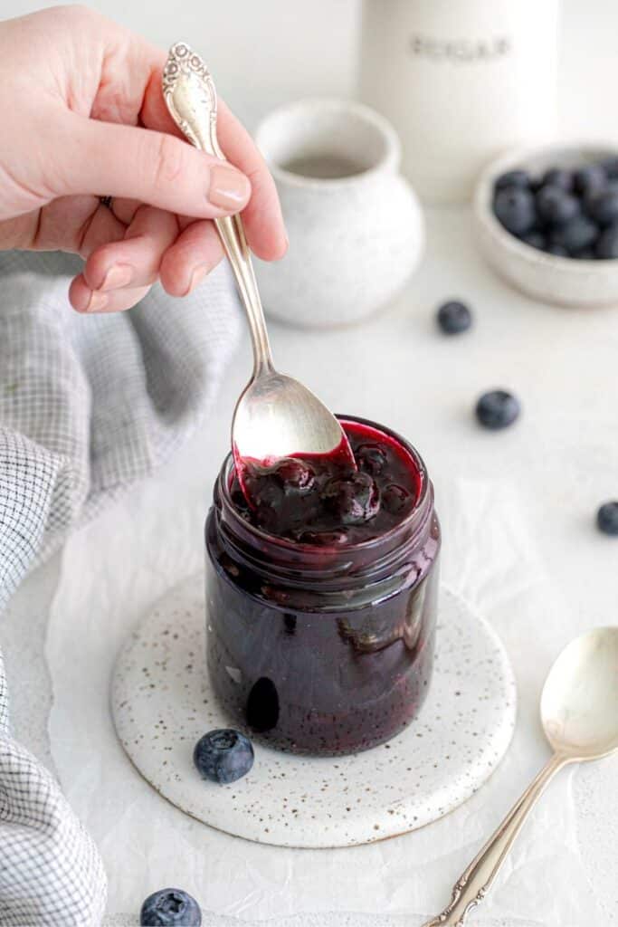 Hand with spoon scooping out some homemade blueberry pie filling from a mason jar.
