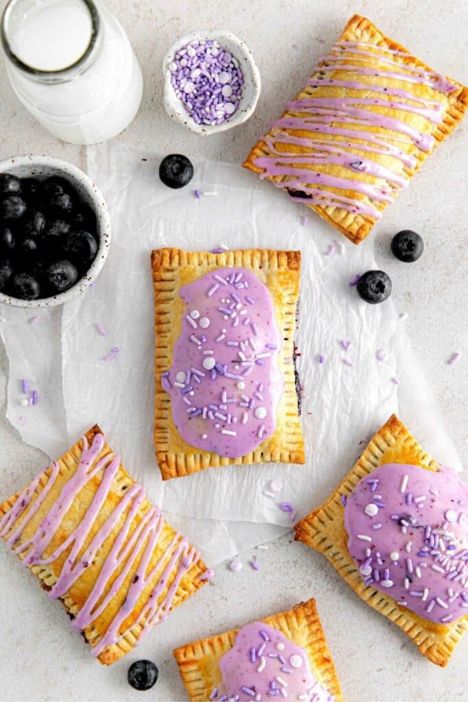 Five homemade blueberry pop tarts on a serving table with fresh blueberries and milk.