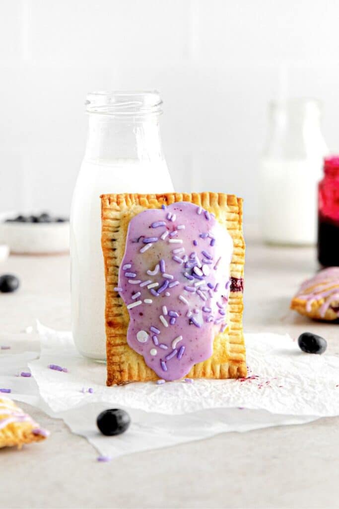 One frosted blueberry hand pie leaning against a small bottle of milk.