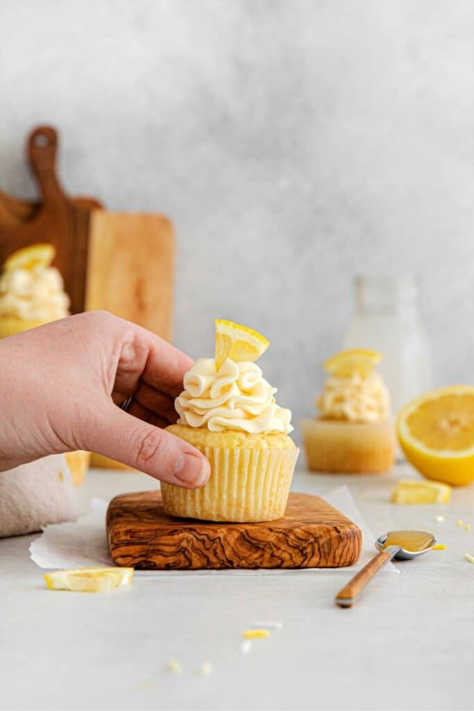 A hand reaching for a lemon cupcake that 's sitting on a wooden board.