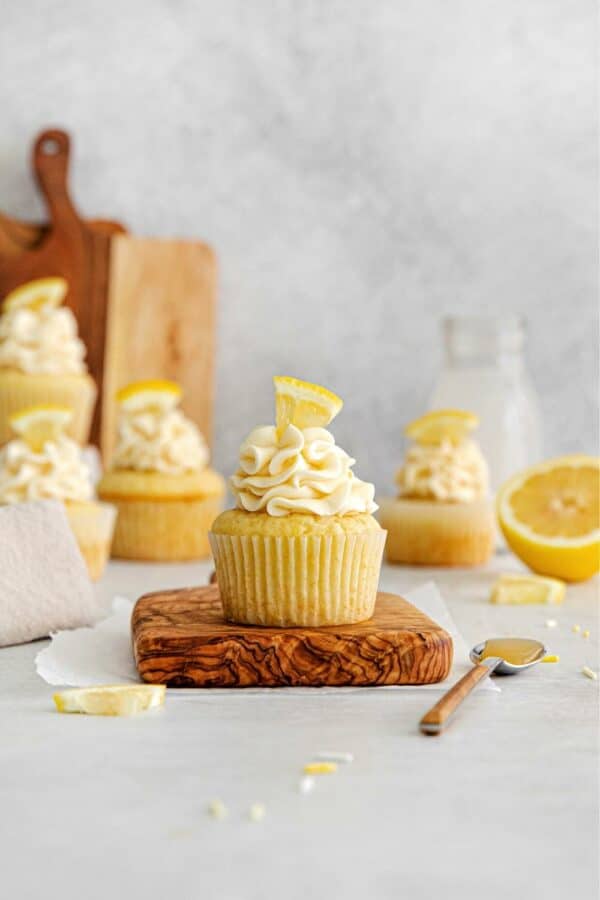 Lemon curd cupcakes with a fresh lemon garnish on a small wooden board.