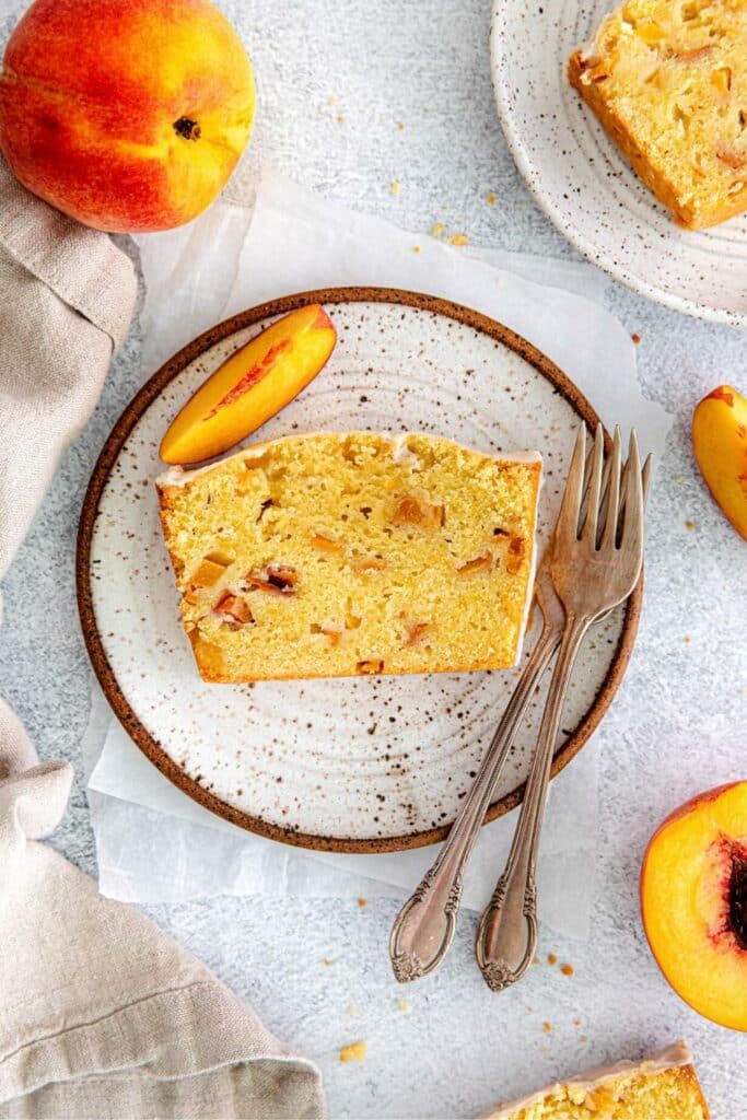 Thick slice of GA peach pound cake on a plate with 2 forks. It's served with fresh peaches.
