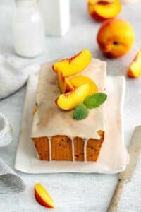 Freshly-glazed loaf of Georgia peach pound cake garnished with 4 fresh wedges of peaches on top.