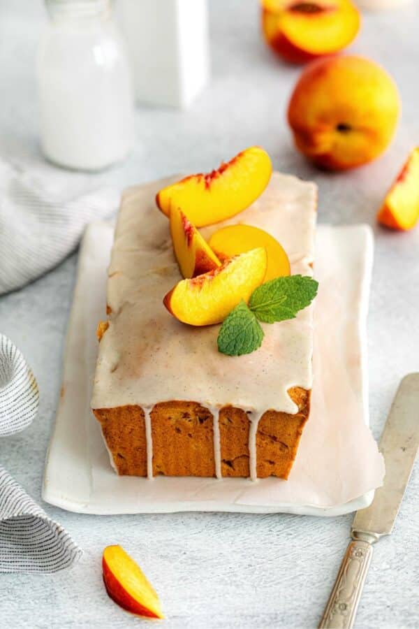 Freshly-glazed loaf of Georgia peach pound cake garnished with 4 fresh wedges of peaches on top.