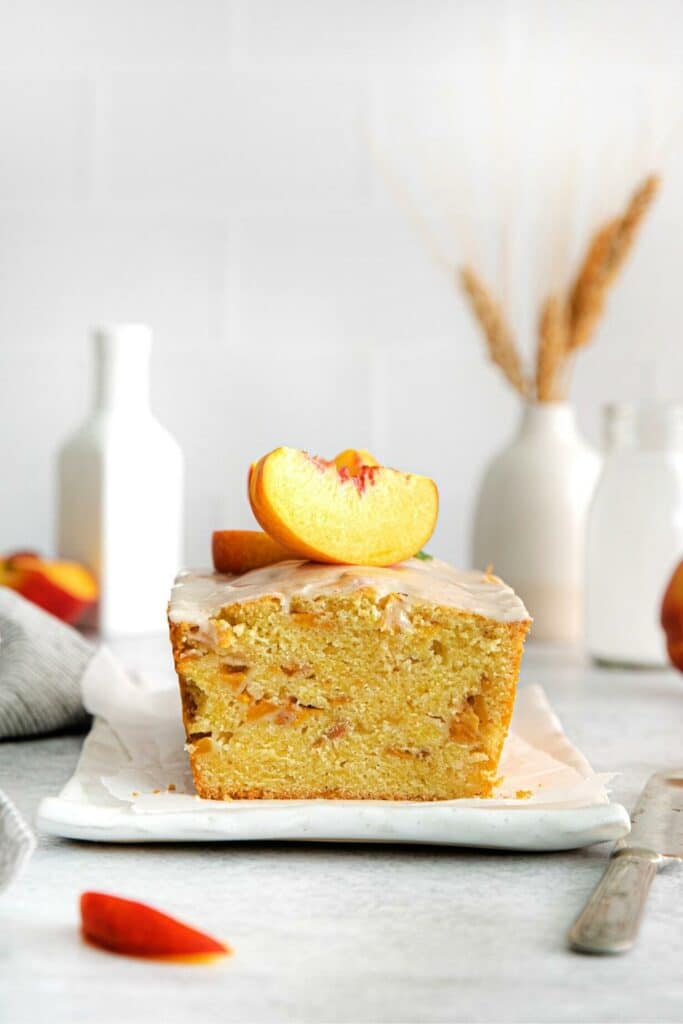 Loaf of peach cobbler pound cake with vanilla glaze and 2 slices of fresh peaches on top.