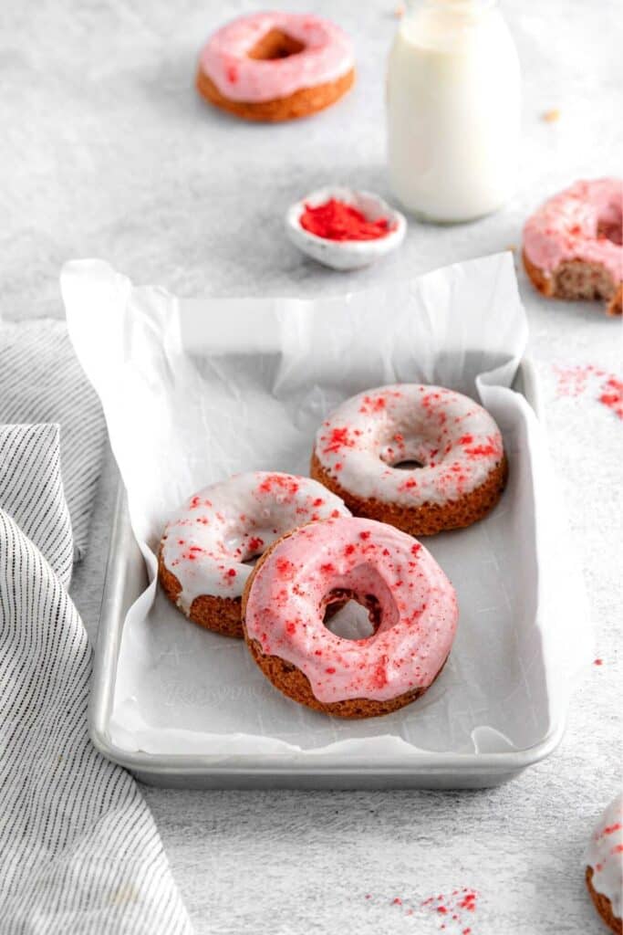 Three strawberry doughnuts with pink and white strawberry glaze garnished with pink bits of ground freeze-dried strawberries.