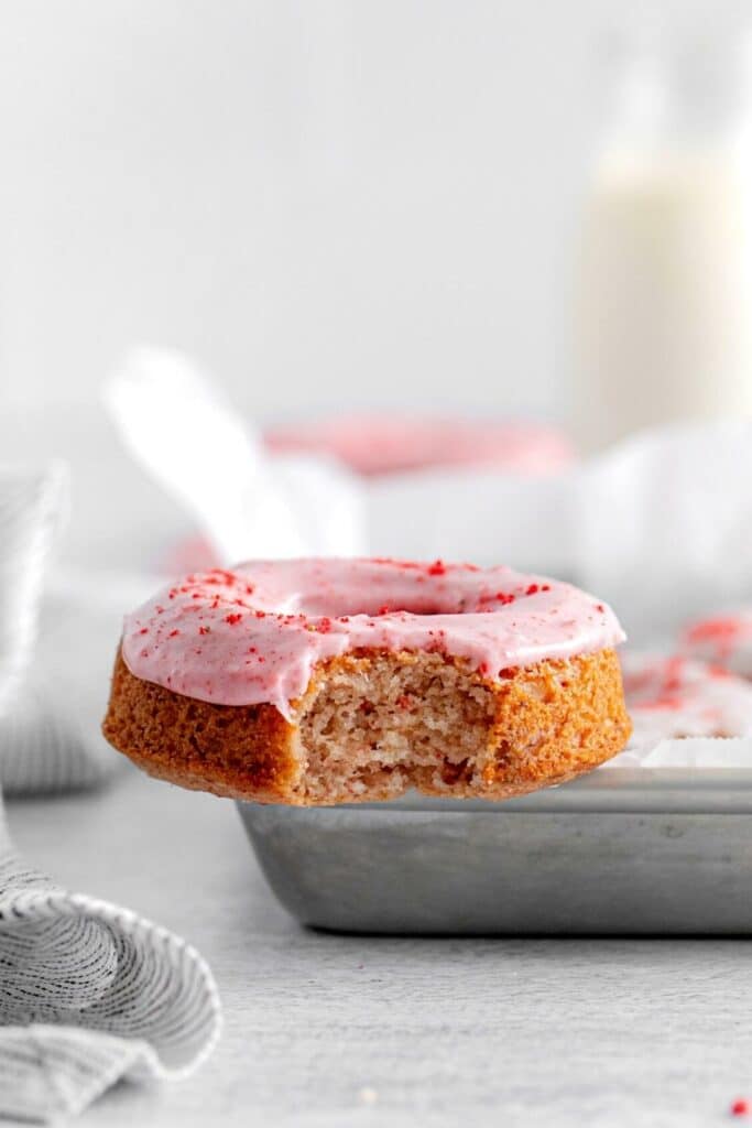 Close-up view of one strawberry frosted donut with a bite taken out. You can see it's tender fluffy texture.
