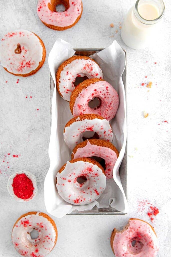 Five DIY Krispy Kreme strawberry doughnuts served in a parchment paper-lined metal loaf pan.
