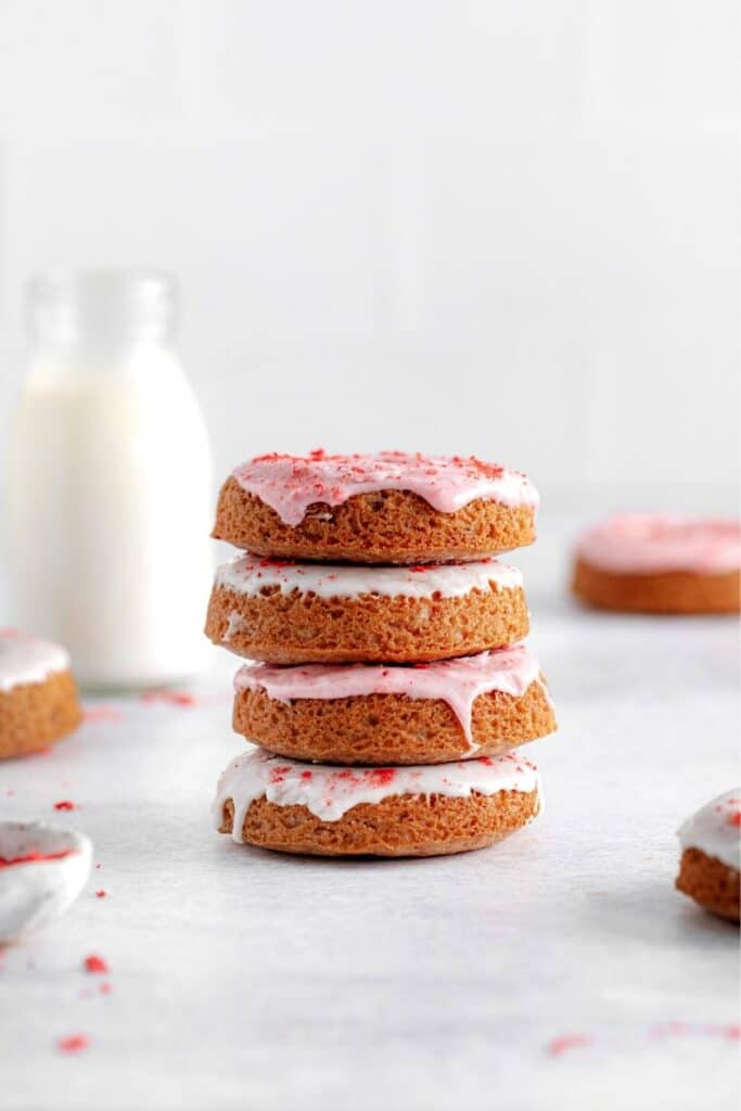 Stack of 4 baked strawberry donuts freshly glazed with a glass bottle of milk in the background.
