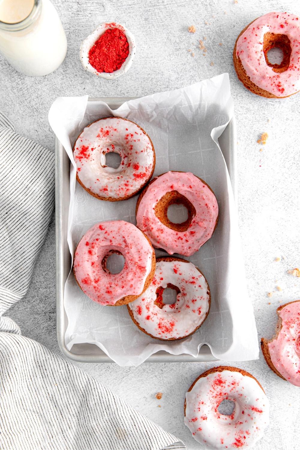 Seven baked strawberry donuts with strawberry donut glaze on a small parchment paper-lined baking tray.