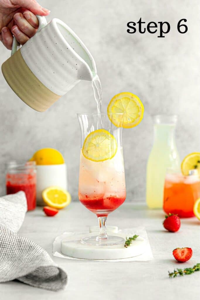 Glass of blended strawberry lemonade being made: hand holding a pitcher of lemonade and pouring it over ice and strawberry syrup.