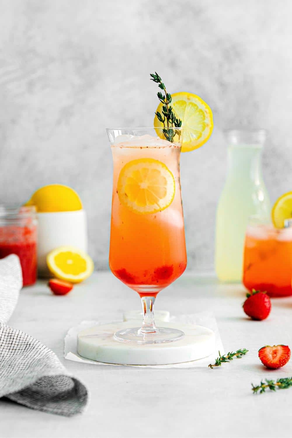 A tall glass of strawberry lemonade garnished with fresh slices of lemon and sprig of thyme.