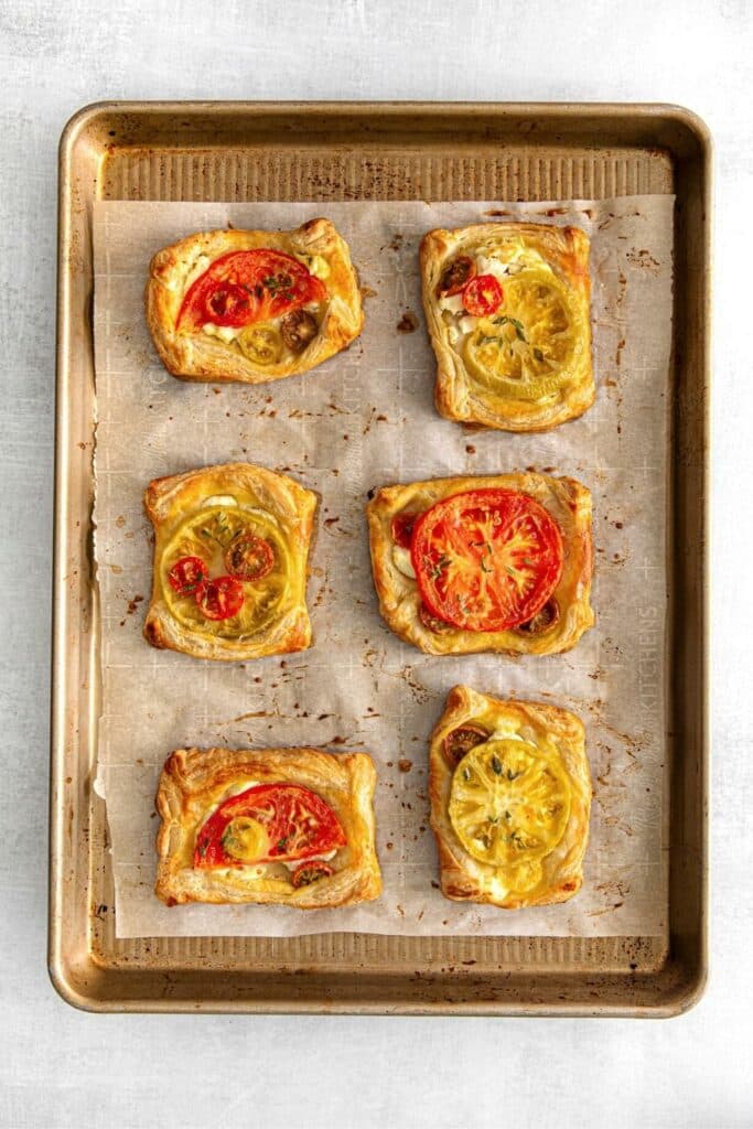 Baking tray with 6 puff pastry tomato tartlets with goat cheese and herbs.