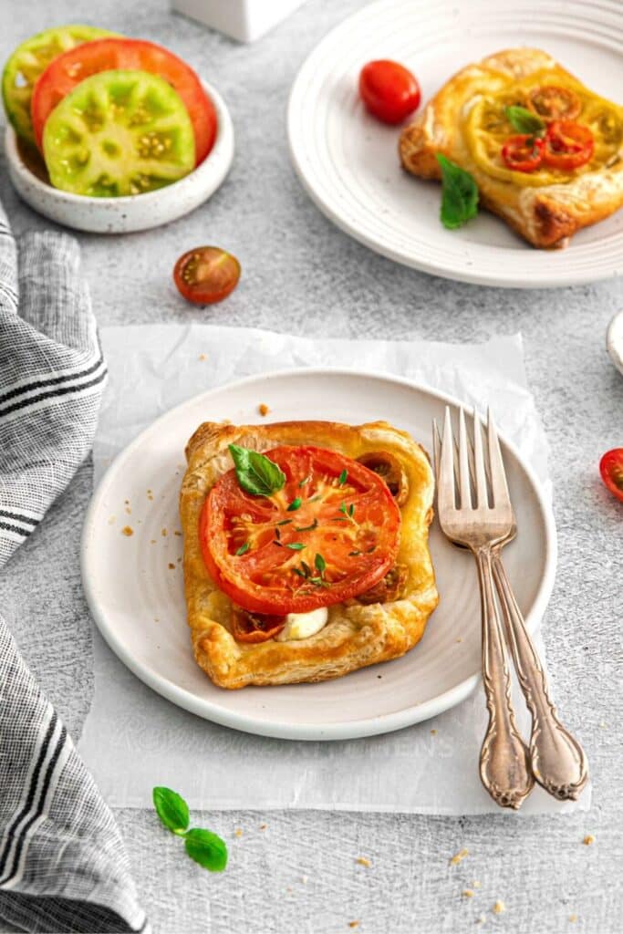 Tomato tart on a plate with forks next to slices of multi-color heirloom tomatoes.