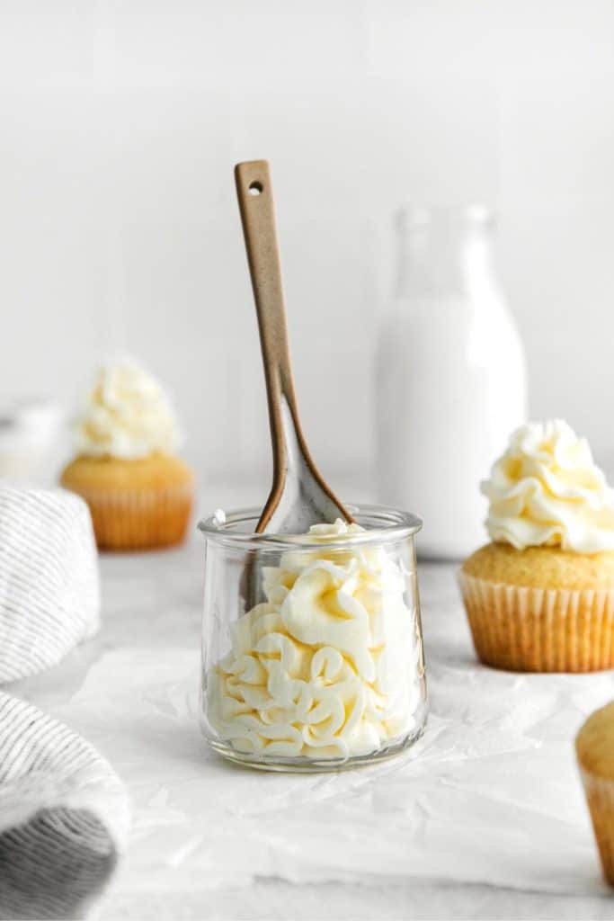 Swirls of fluffy vanilla buttercream piped into a small glass jar with a spoon in it.