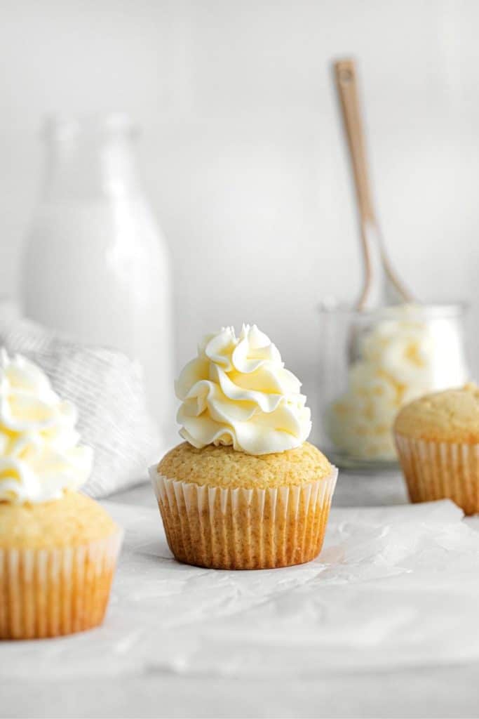 White vanilla cupcake frosted with tall swirls of vanilla buttercream next to a glass bottle of milk.