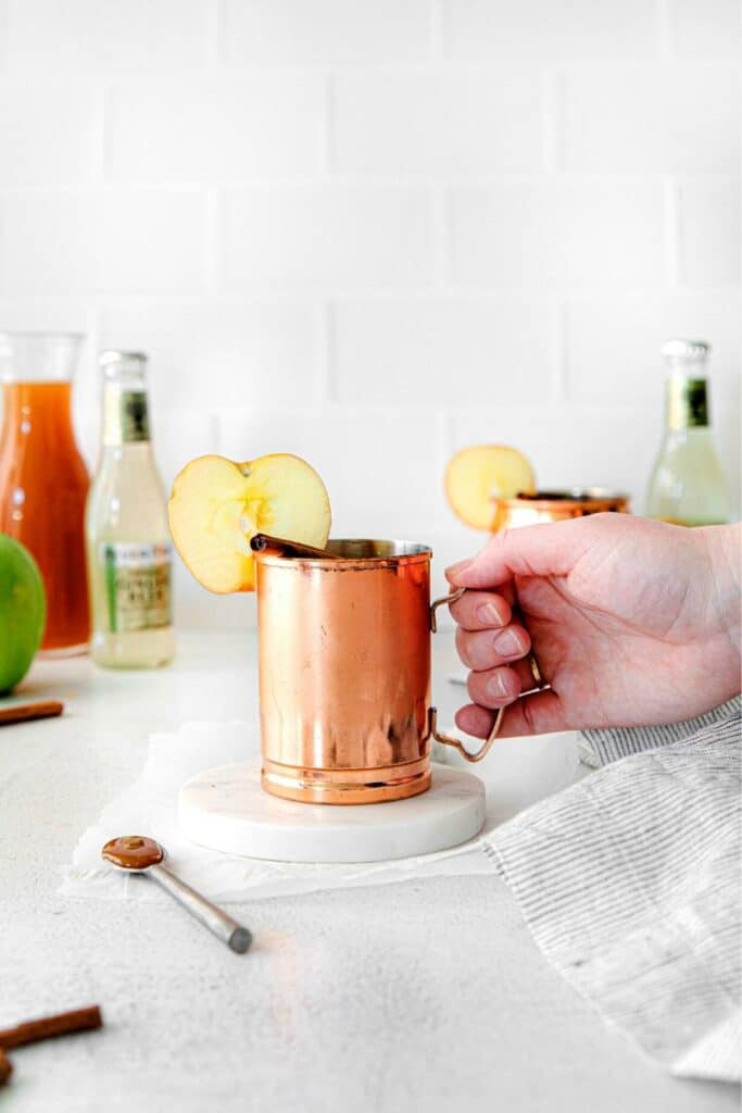 A hand lifting a apple cider mule in a copper mug.