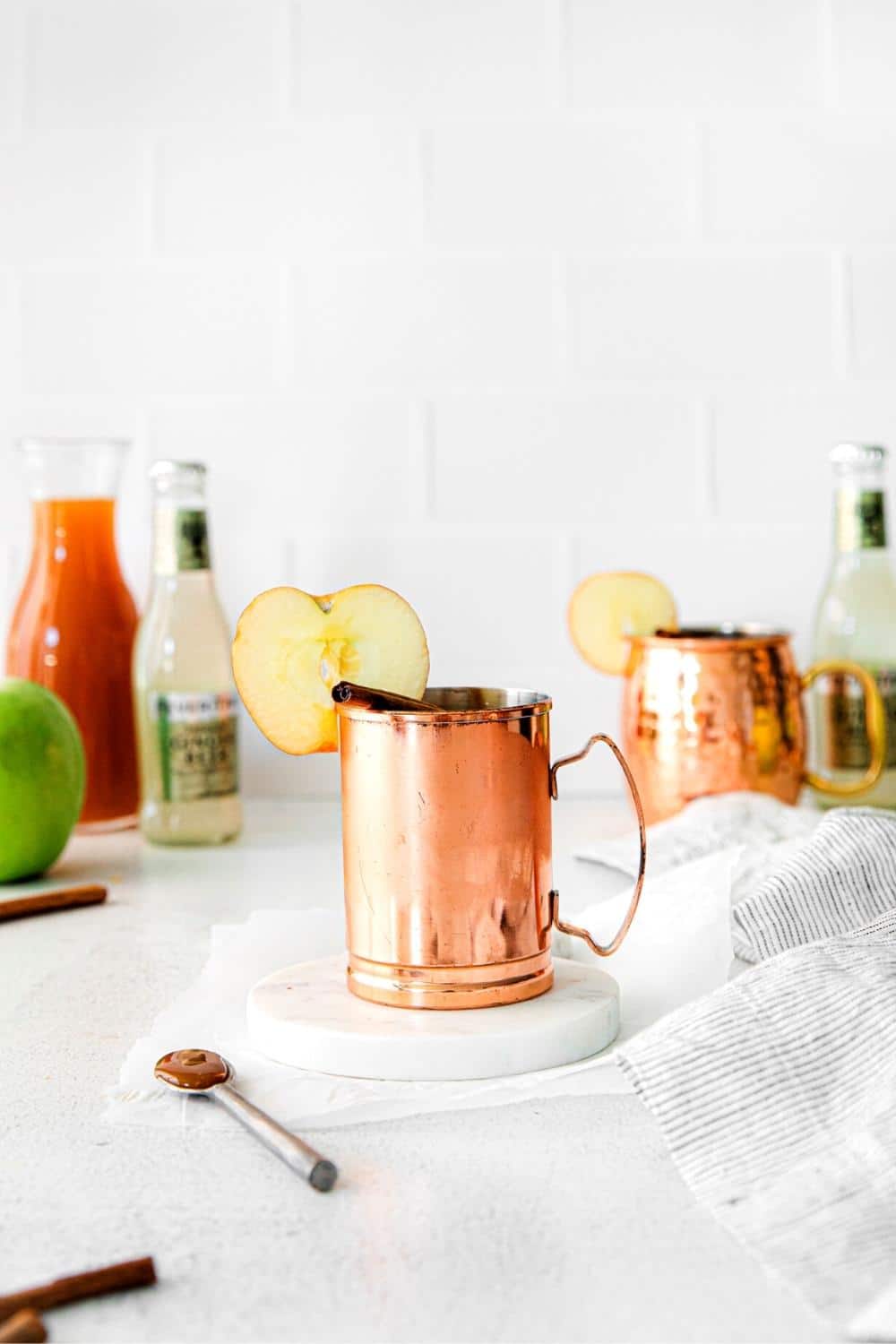 A Moscow Mule Drink garnished with an apple slice and cinnamon stick, and drizzled with salted caramel sauce.