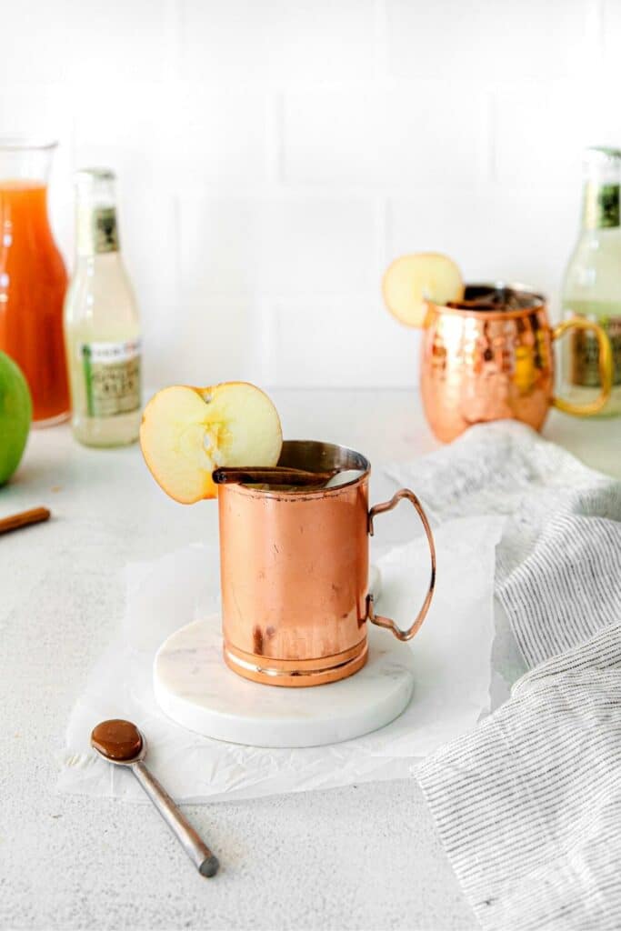 An apple cider mule drink in a shiny copper mug garnished with an apple slice.