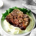 Slice of BBQ meatloaf with savory meatloaf glaze served over mashed potatoes and side of arugula.