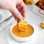 A genuine CFA waffle potato fry being hand dipped into homemade Chick-Fil-A dipping sauce.