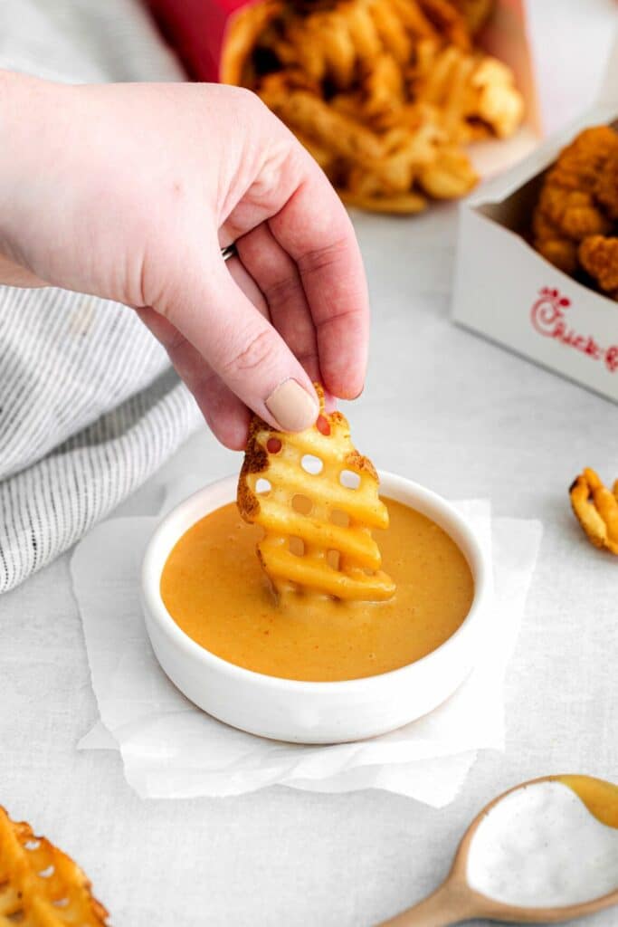 Hand dipping a CFA waffle fry into copycat Chick-Fil-A sauce.