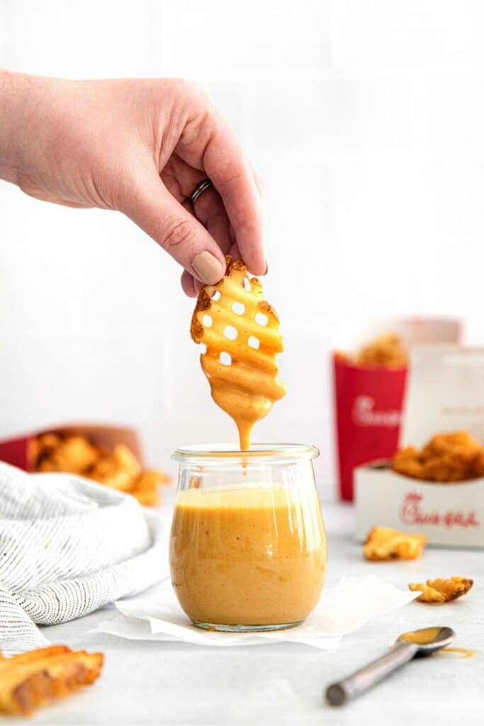Hand holding and dipping a real Chick-Fil-A waffle fry into copycat Chick-Fil-A sauce.