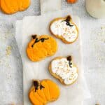 Eight iced pumpkin sugar cookies in pumpkin shapes frosted in orange and white.