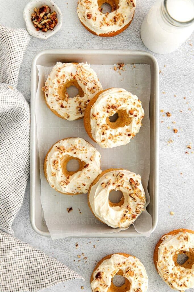 Glazed maple donuts served on a parchment paper-lined baking tray with a glass bottle of milk.