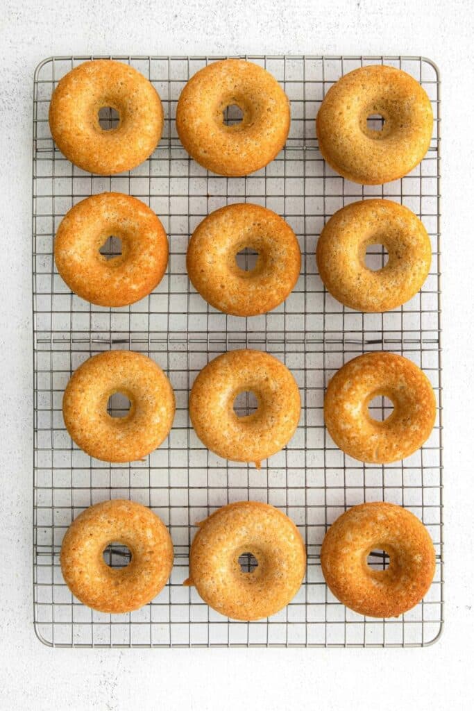 One dozen freshly-baked maple donuts cooling on a wire rack.